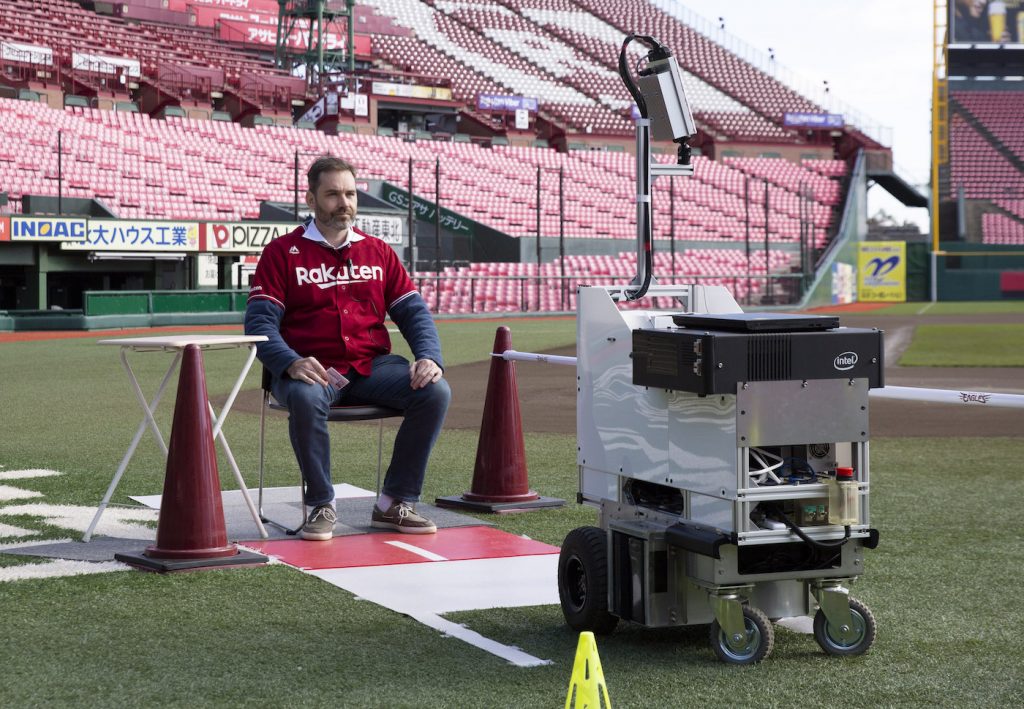 An unmanned delivery robot brings a package to a member of staff on the field.